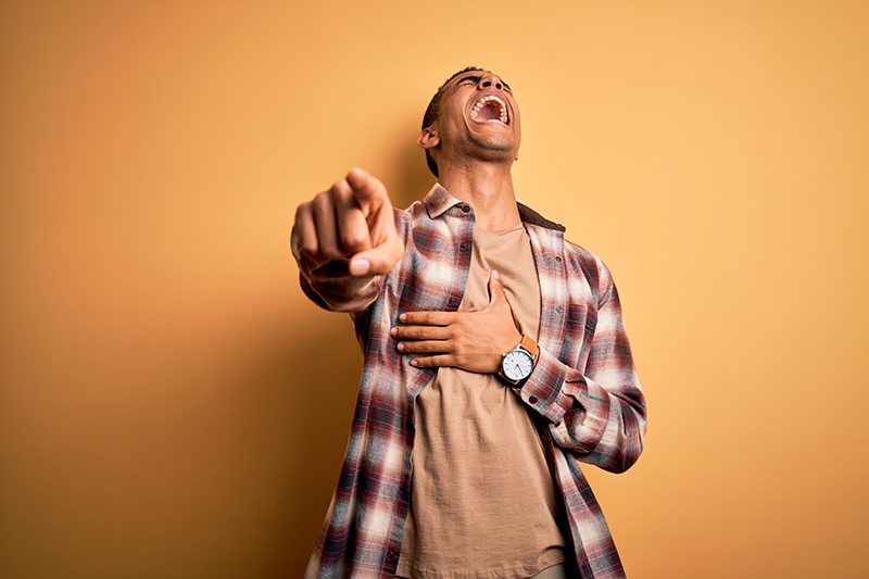 Young handsome african american man wearing casual shirt standing over yellow background laughing at you, pointing finger to the camera with hand over body, shame expression