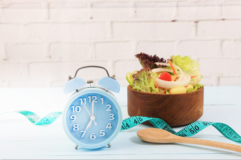 Selective focus Alarm of blue clock with Intermittent fasting and Healthy food and salad  as measuring tape for diet diary on wooden background